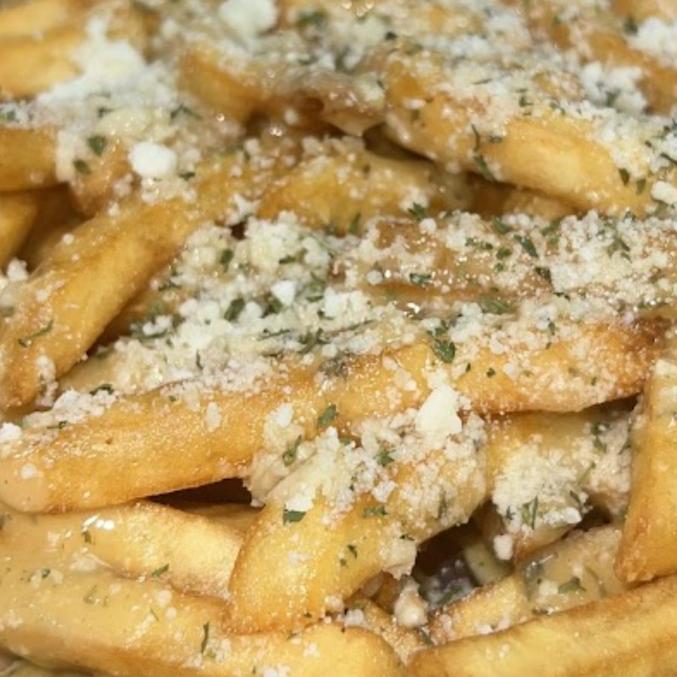 Close-up of golden french fries generously topped with grated cheese and herbs.