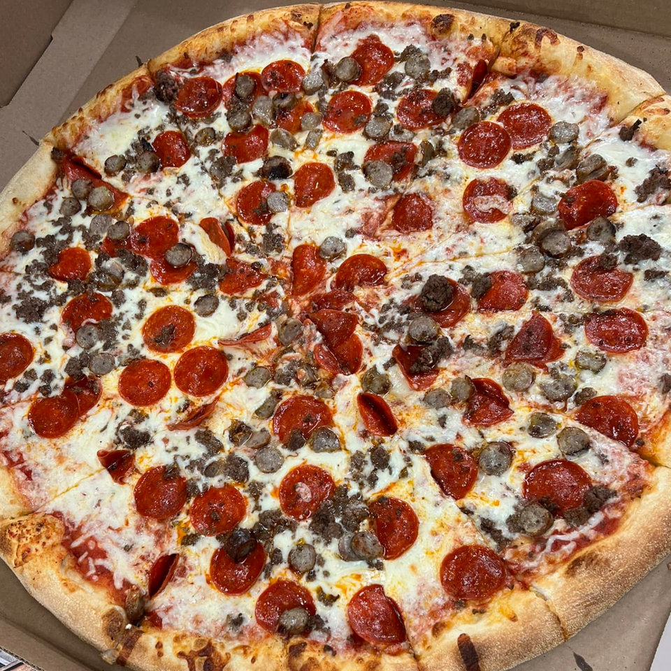 A whole Sal's Pizzeria pizza, topped with pepperoni, sausage, and ground beef, in a cardboard box.