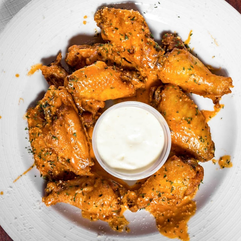 A plate of Sal's Pizzeria's buffalo wings, coated in orange sauce and herbs, with a side of ranch.