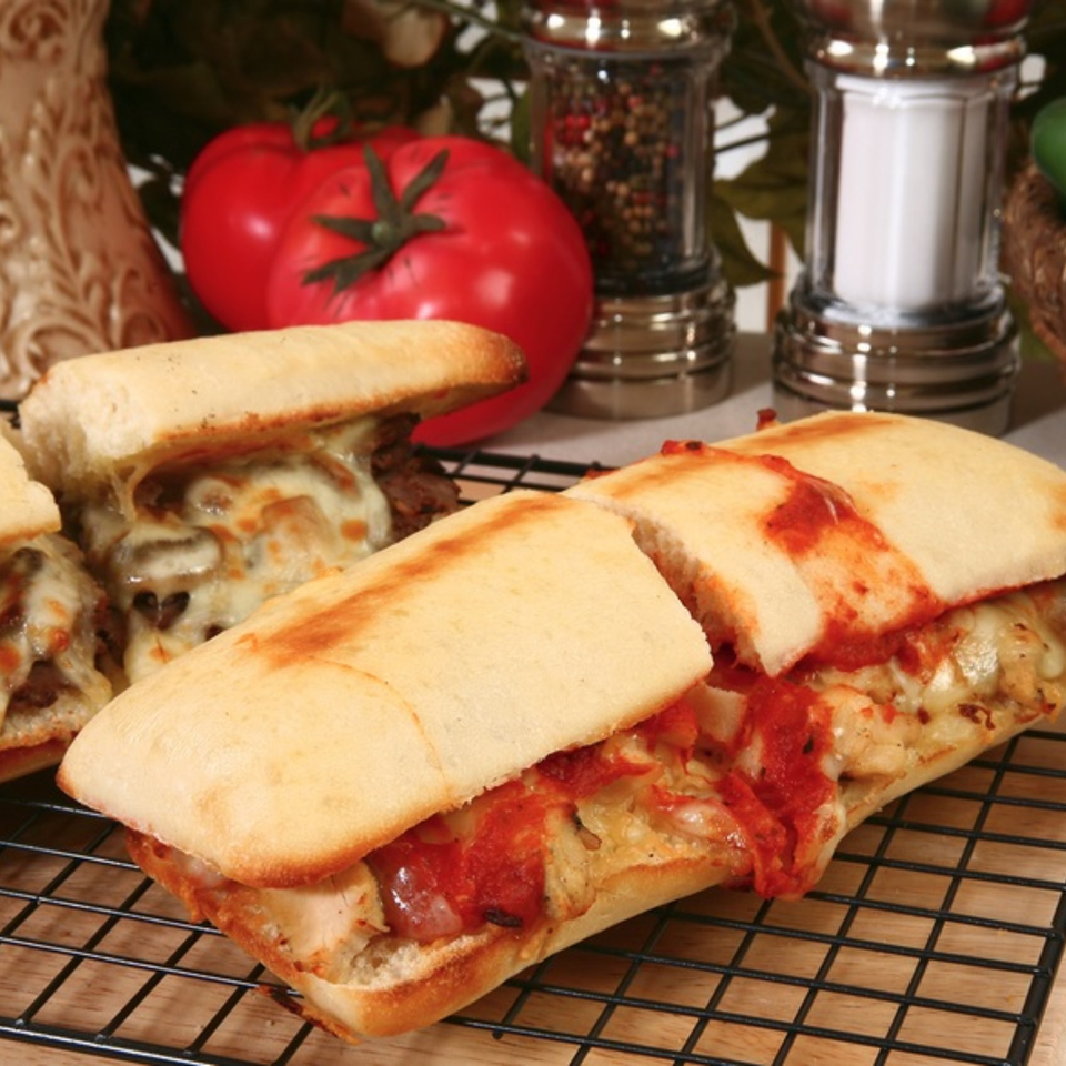 Two cheesy Sal's Pizzeria sandwiches with red sauce and meat on a cooling rack.